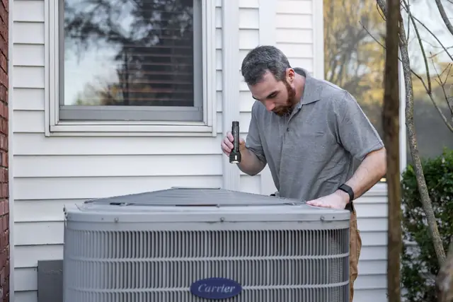 Technician inspecting a condensing unit next to a house