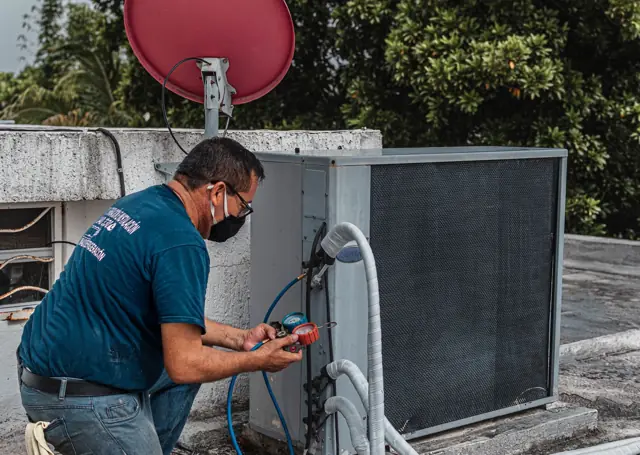 Technician reading gauges at a rooftop condensing unit