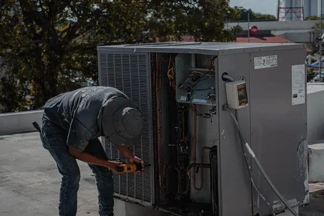 Technician testing parts inside an open outdoor heat pump cabinet