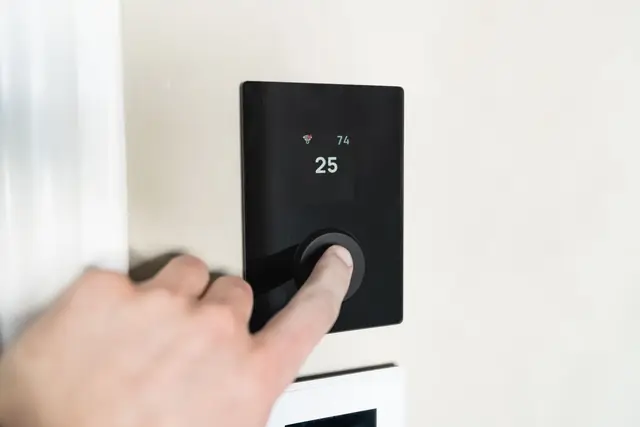 Finger pressing the dial on a digital wall thermostat