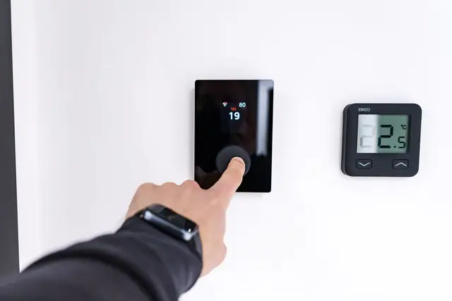 Hand setting a black digital thermostat on a white wall